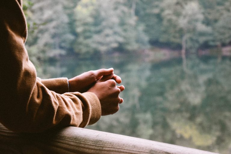 Eine Person lehnt mit den Unterarmen auf einem Geländer und blickt in die Natur. Kümmern sie um Ihre Mental Health – mit der Unterstützung von fortschritt